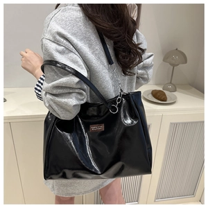 Detail of a black glossy tote bag featuring a metallic chain strap and a leather logo patch