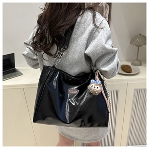 Detail of glossy black patent leather tote bag with chain strap and plush pendant