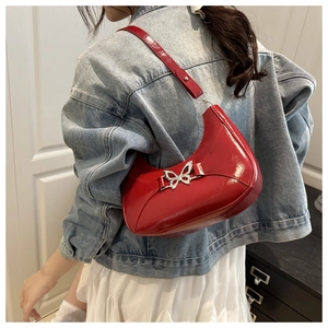 Sac demi-lune rouge en cuir verni avec boucle papillon argentée porté à l'épaule