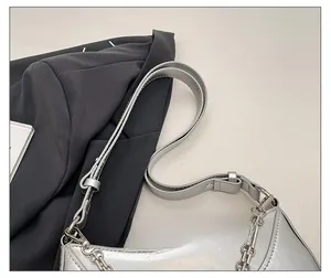Detail of adjustable leather strap and silver metal chain on shiny shoulder bag