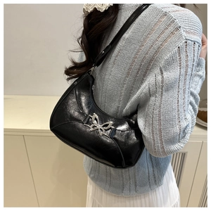 Détail d'un sac demi-lune noir avec boucle papillon métallique porté à l'épaule pour femme
