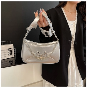 Détail d'un sac hobo argenté métallisé avec boucle papillon et chaîne décorative
