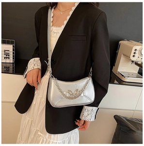 Detail of silver metallic butterfly chain bag worn by a model in a trendy cafe setting