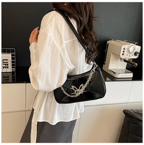 Modèle portant un sac d'épaule en cuir verni noir avec chaîne papillon argentée