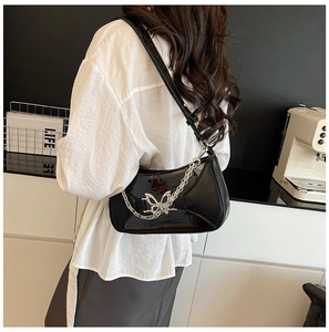 Detail view of black patent leather bag with silver butterfly buckle and chain on shoulder