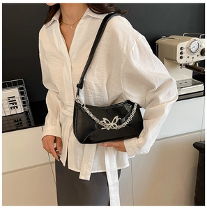 Détail du sac en cuir verni noir avec boucle papillon argentée et chaîne en métal épais