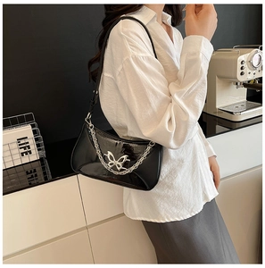 Gros plan d'un sac bandoulière en cuir verni noir avec papillon argenté et chaîne métal