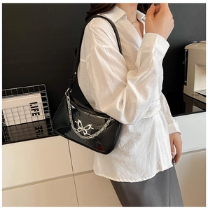Détail du sac baguette en cuir verni noir avec grand papillon argenté et chaîne métal