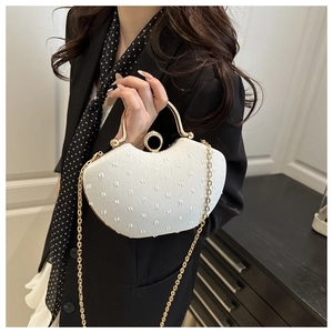 Detail of white shell-shaped clutch with pearl texture and gold ring handle worn with blazer