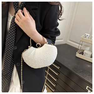 Detail of white shell-shaped evening bag with pearl texture and gold circular handle