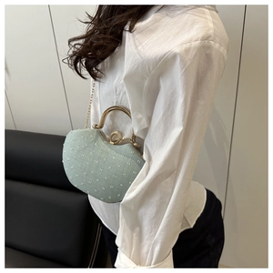 Detail of mint green heart-shaped clutch with gold handle and delicate chain strap