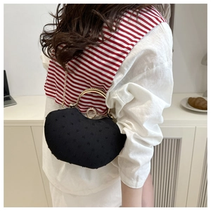 Detail of black textured evening bag with golden circular handle and elegant metal chain