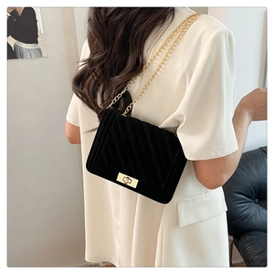 Détail d'un sac bandoulière noir matelassé avec chaîne dorée sur un blazer blanc