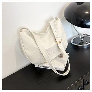 Detail showing creamy white minimalist shoulder bag with gold buckle and side lettering