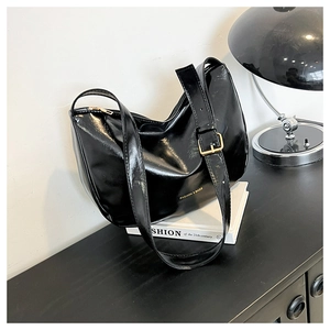 Detail of black glossy leather tote bag with gold adjustable buckle and logo print