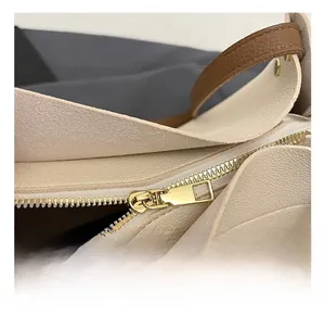 Close-up of premium gold-tone metal zipper and brown leather strap on cream tote bag