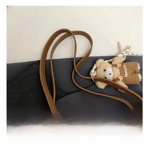 Detail view of beige tote bag shoulder strap featuring a fashion bear plush pendant