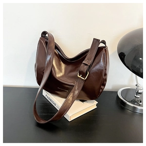 Close-up of dark brown glossy patent leather shoulder bag with adjustable strap and buckle