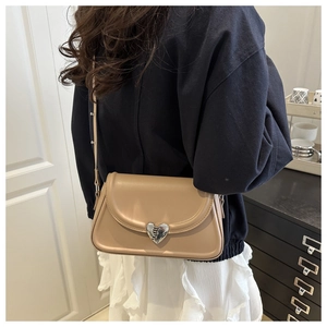Detail of minimalist beige saddle bag featuring a silver heart-shaped metal buckle on the flap