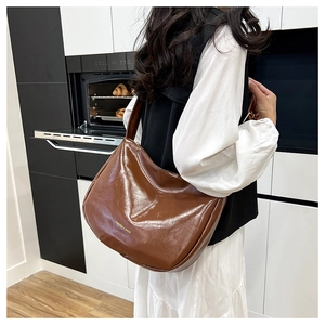 Brown vintage hobo bag with glossy finish and wide strap shown on a shoulder