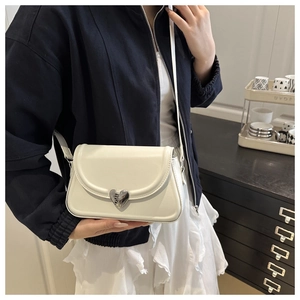 Close-up of cream-colored crossbody bag featuring a silver heart-shaped metal buckle detail