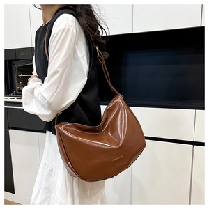 Close-up of brown semi-circle shoulder bag with gold lettering on glossy PU leather