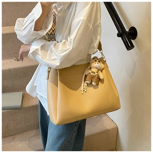 Detail of yellow tote bag featuring a geometric woven strap and cute plush bear charm