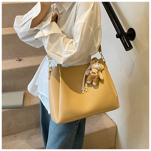 Detail of a large khaki tote bag with a cute bear charm and golden metal hardware