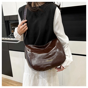 Detail of dark brown glossy patent leather tote bag with gold logo in daily use