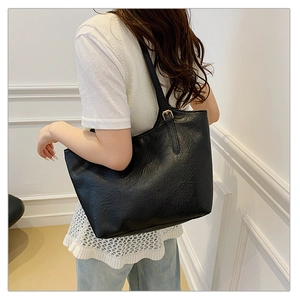 Detail of black leather tote bag with gold buckle on shoulder strap and textured finish