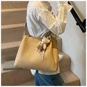 Close-up of beige large tote bag with plush bear charm on a model in casual setting