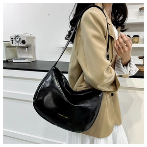 Detail of a black shiny faux leather hobo shoulder bag with gold text on beige coat