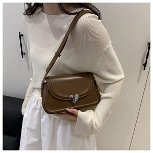 Detailed view of brown leather bag with silver heart-shaped lock on white outfit