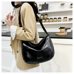 Glossy black underarm bag with gold lettering shown on model in a chic cafe setting