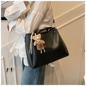 Detail of a large black leather tote bag with gold hardware and a cute bear charm accessory