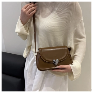 Detail of a brown leather shoulder bag featuring a silver heart-shaped magnetic buckle