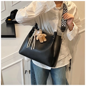 Close-up of black tote bag with patterned strap and cute bear charm worn by a model