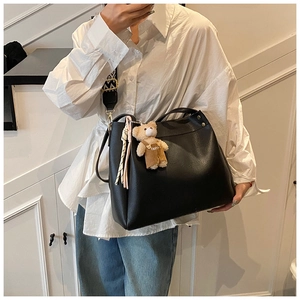 Detail view of a black tote bag with geometric wide strap and cute bear charm accessory