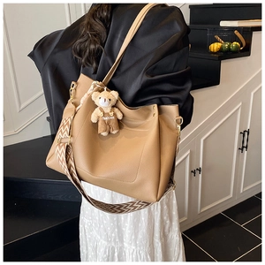 Detail of camel lychee leather tote bag with woven shoulder strap and bear charm