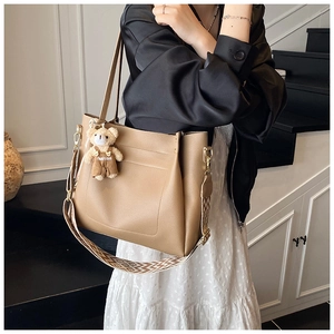 Detail of khaki tote bag with wavy strap and plush bear charm for daily commute