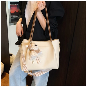 Detail of off-white tote bag with wave-textured strap and plush bear charm on model