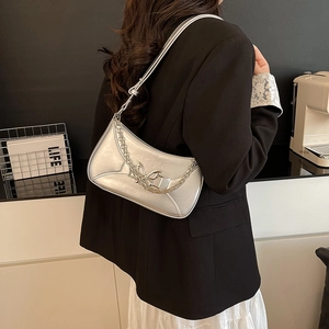 Sac à bandoulière argenté avec boucle papillon et chaîne en métal porté par un mannequin