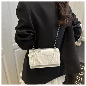 Detail of white woven crossbody bag with pearl bow decoration and silver chain strap