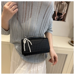 Close-up of black woven shoulder bag with pearl bow and silver handle on model