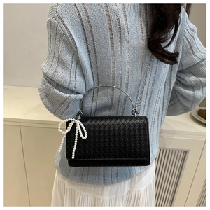 Detail of woven black leather handbag with silver metallic handle and pearl bow charm