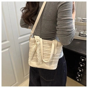 Detailed side view of woven straw tote bag with lace ribbon and cream leather strap