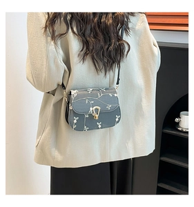 Detail view of a gray crossbody bag featuring intricate white floral embroidery and gold clasp