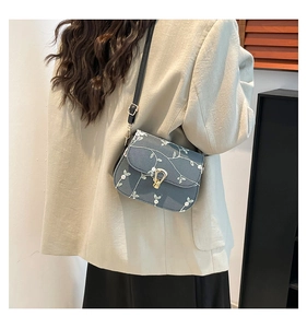 Detail of blue canvas crossbody bag with white flower embroidery and gold U-buckle