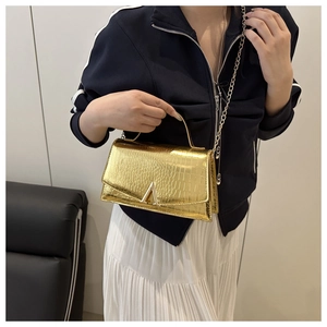 Detail of gold crocodile embossed crossbody bag with metallic V-clasp and chain strap