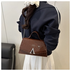 Detail of dark brown croc-effect leather square bag with silver V-shaped buckle